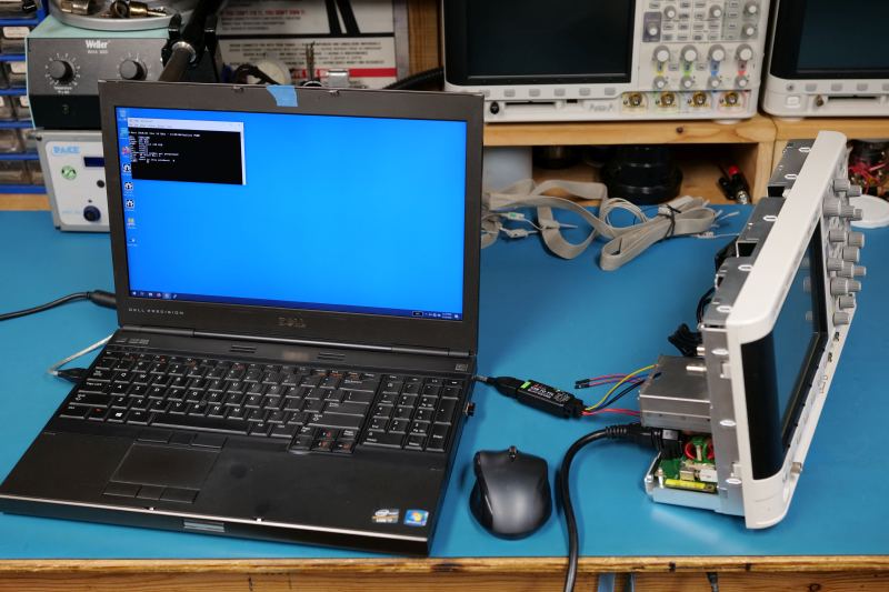 Oscilloscope, old laptop and UART cable setup on workbench.